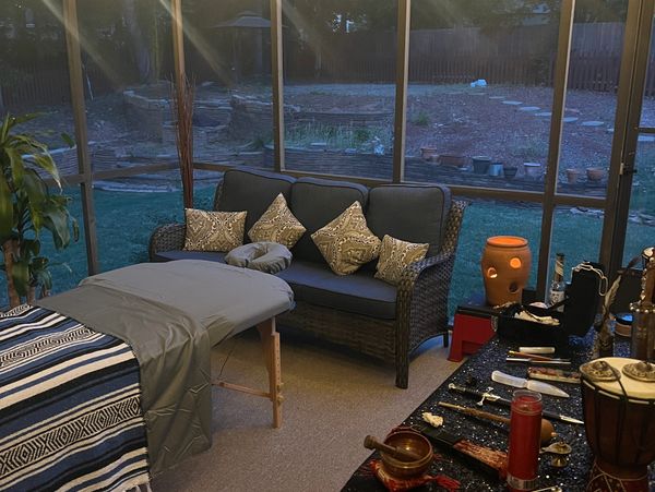Cozy indoor massage setup with a sofa, massage table, and ritualistic items on a table.