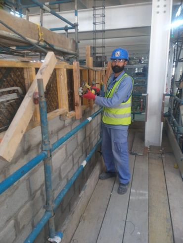 Construction worker wearing safety gear using a power tool on a wooden structure.