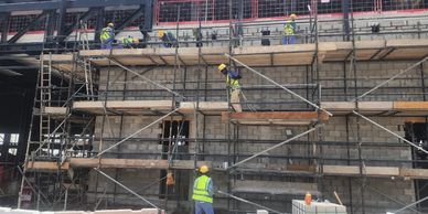 Construction workers wearing safety gear work on scaffolding around a brick building.