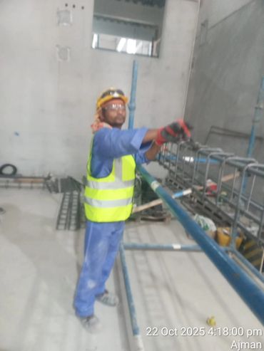 Construction worker in safety gear handling metal framework indoors.
