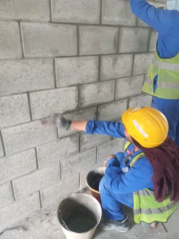 Construction worker applying mortar to a concrete block wall.