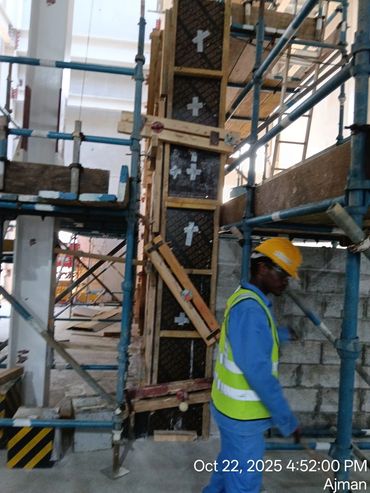 Construction worker in safety gear at a building site with scaffolding and concrete formwork.