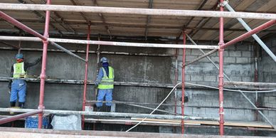Two construction workers plastering a wall on scaffolding at a building site.