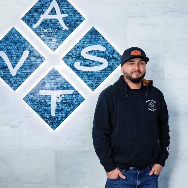 Man in casual outfit stands beside illuminated blue mosaic letters on a wall.