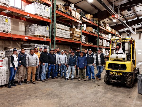 A group of warehouse workers posing with a forklift inside a storage area.