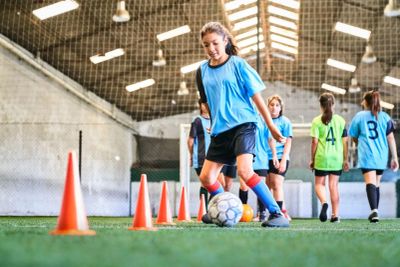Girl practicing soccer dribbling indoors.