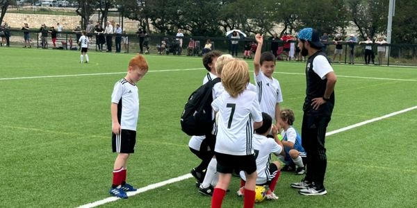 Youth soccer team gathers around coach on the field during a match.