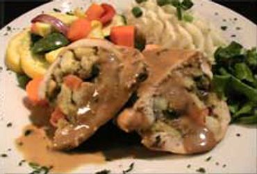 Stuffed chicken breasts with gravy, mashed potatoes, and mixed vegetables on a plate.