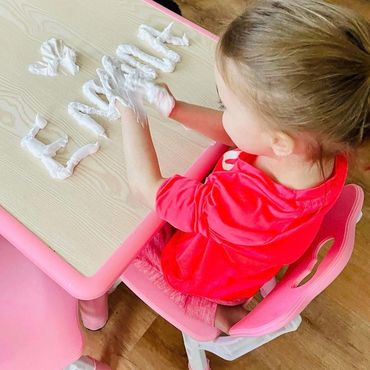 Child sitting at table writing her name with shaving cream