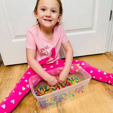 Young girl sitting on the floor playing with a bin full of water beads