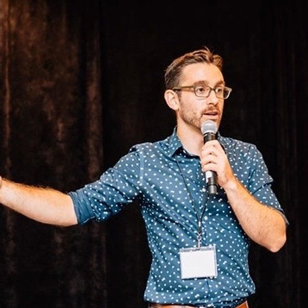 A white man with short brown hair speaks on a microphone 