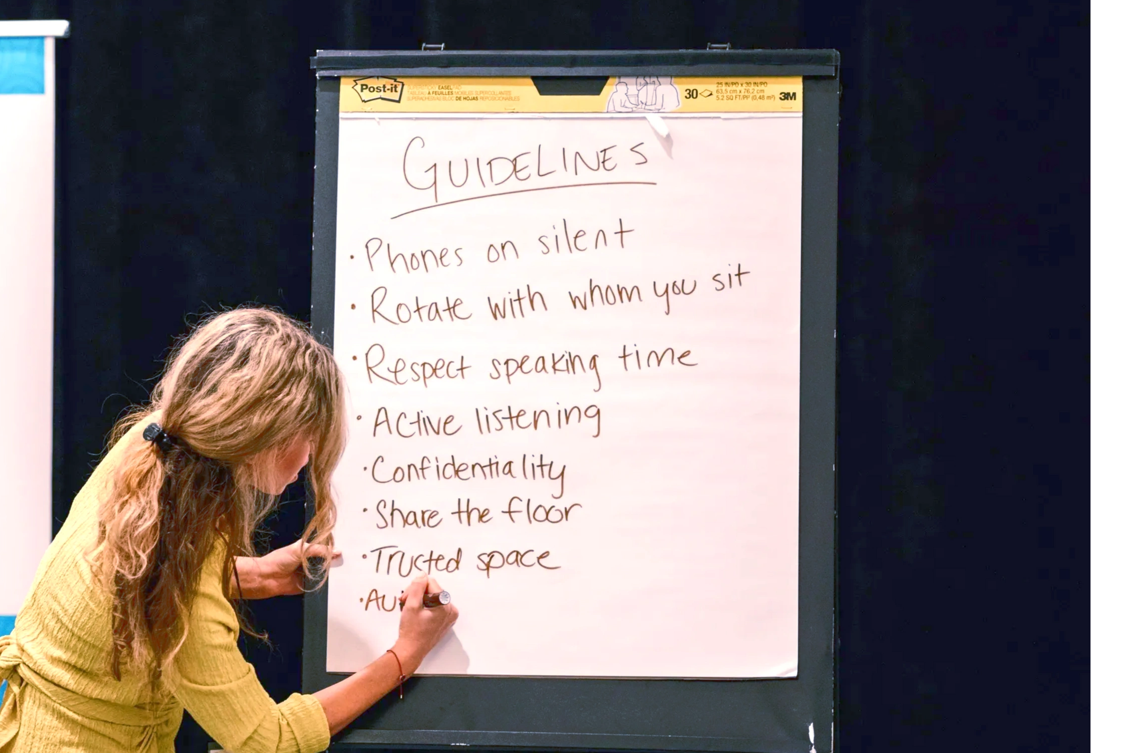 A woman writes on Marge white flip chat paper “group guidelines” 