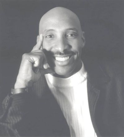 Smiling man in a black jacket and white shirt posing thoughtfully.
