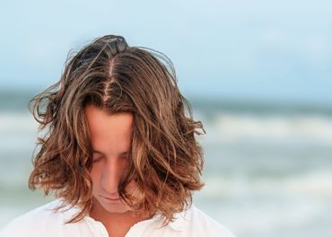 Young man with long wavy hair looking down at the beach.