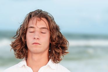Young man with closed eyes and shoulder-length hair by the sea.