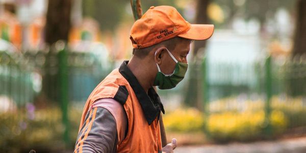 A sanitation worker in orange uniform cleaning the street with a broom.
