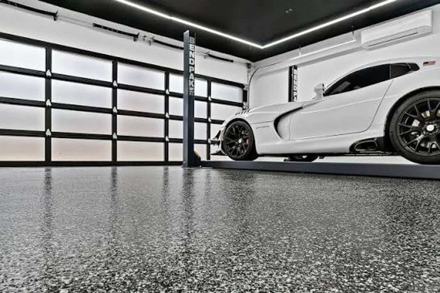 A sleek white sports car elevated in a modern garage with polished speckled flooring.