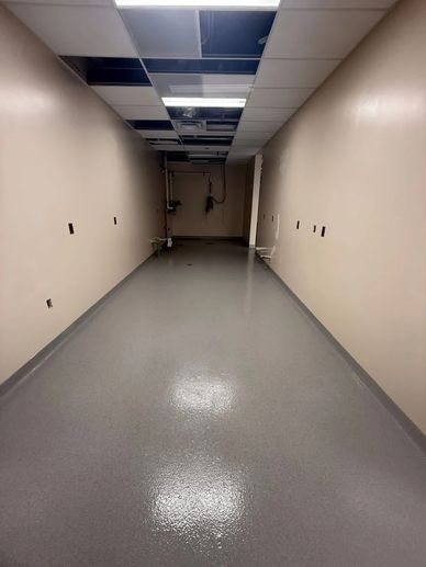 Empty hallway with beige walls and a shiny gray floor under repair.