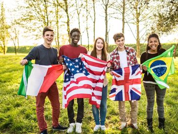 Five young people holding various international flags outdoors, smiling happily.