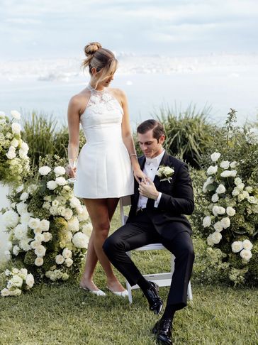 Bride in a white dress and groom in tuxedo share a tender moment outdoors.