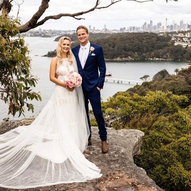 Bride and groom posing on a cliff with a scenic city and water backdrop.