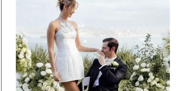 Groom kissing bride's hand at outdoor wedding.