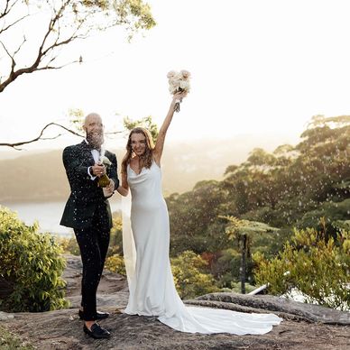 Newlywed couple celebrating with champagne outdoors at sunset.