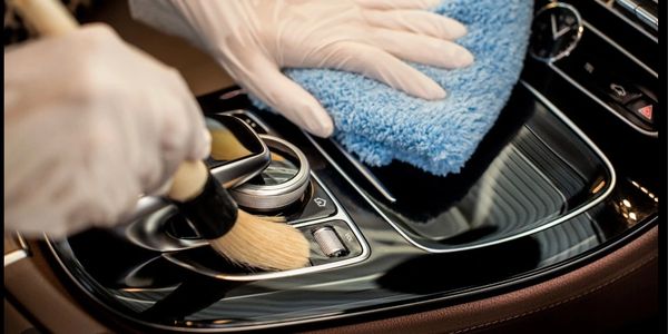 Person cleaning car interior with brush and cloth.