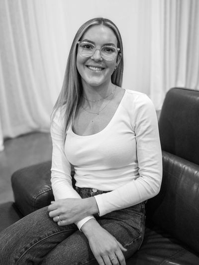 Smiling woman with glasses sits on a leather couch in a casual setting.