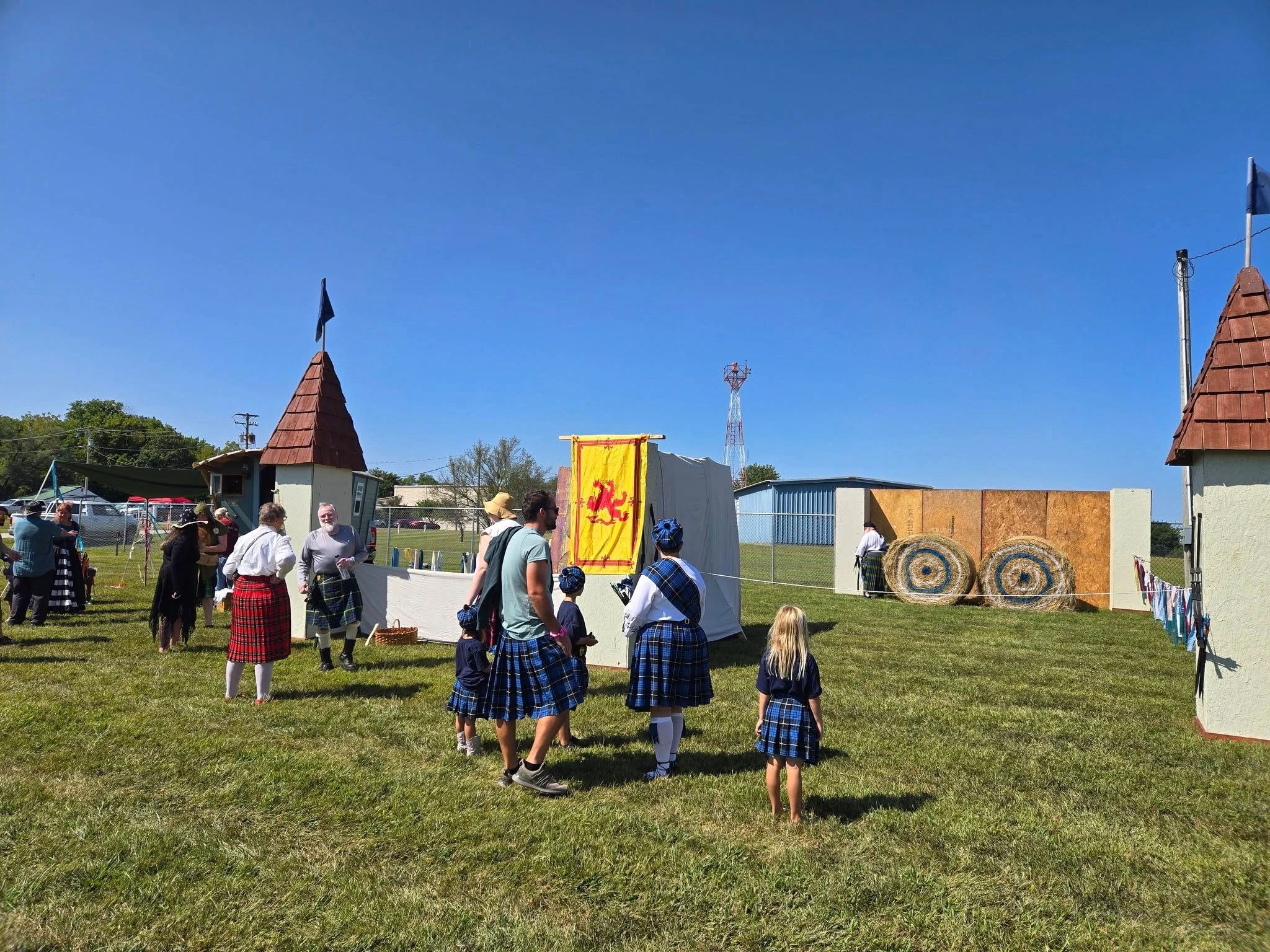 People in kilts at a Scottish festival with archery targets and medieval decorations.