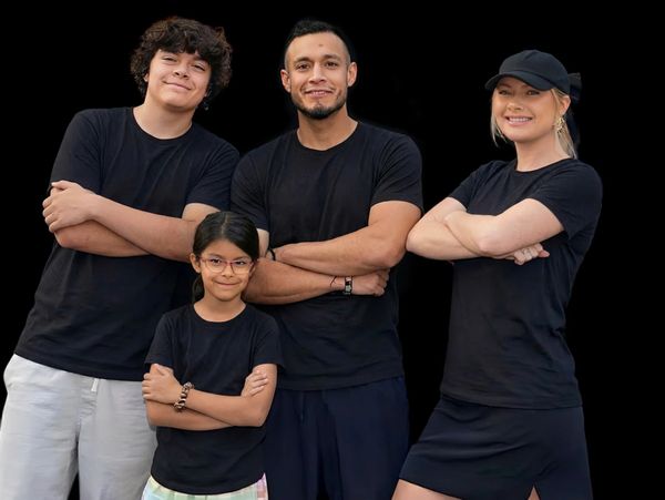 Four people wearing black shirts pose confidently with arms crossed against a black background.