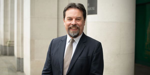 Man in a suit smiling outside a building with columns.