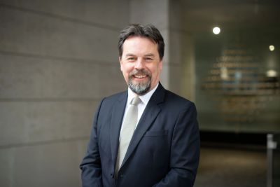 Smiling middle-aged man in a suit and tie standing indoors.