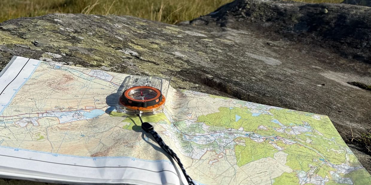 A compass resting on a detailed topographic map on a rock outdoors.