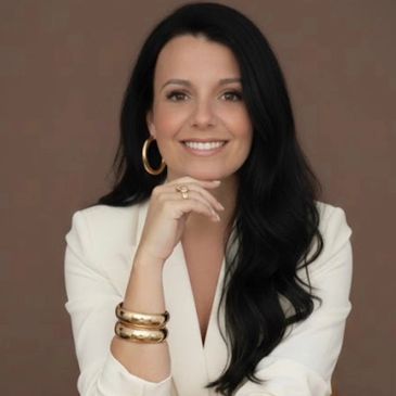 Confident woman with black hair in white outfit and gold accessories.