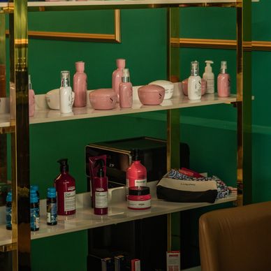 A variety of pink and white cosmetic containers on a white shelf with a green background.