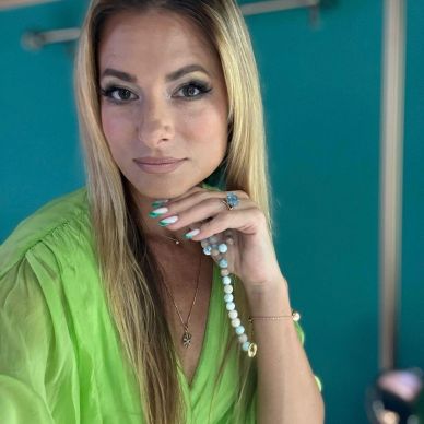 Frau mit grüner Bluse und Perlenkette posiert vor blauem Hintergrund.