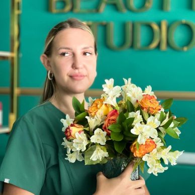 A woman in green holding a colorful bouquet of flowers.