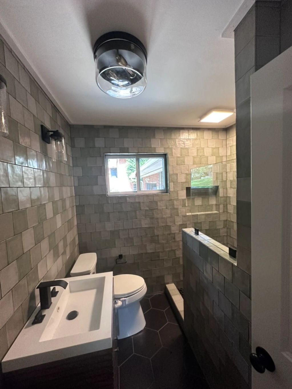 green subway tile bathroom with clear glass light and black hexagon tiles