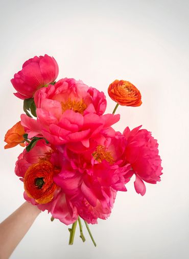 A vibrant bouquet of pink peonies and orange ranunculus flowers.
