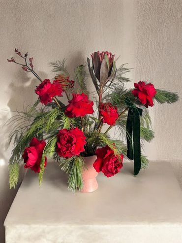 Elegant floral arrangement with red roses and greenery in a pink vase.