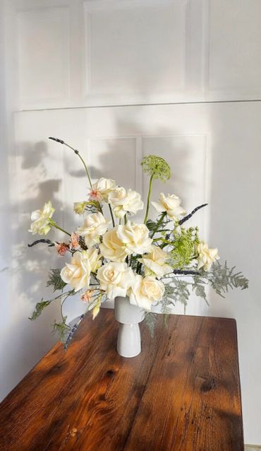 Elegant white floral arrangement in a modern vase on wooden table.