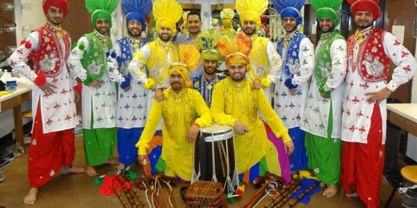 A group of men in colorful traditional Punjabi attire posing with musical instruments.