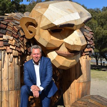 Man posing with a large wooden sculpture of a humanoid figure.