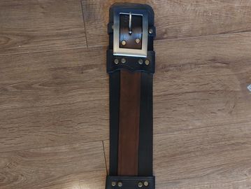A brown and black leather belt with a square metal buckle on a wooden floor.