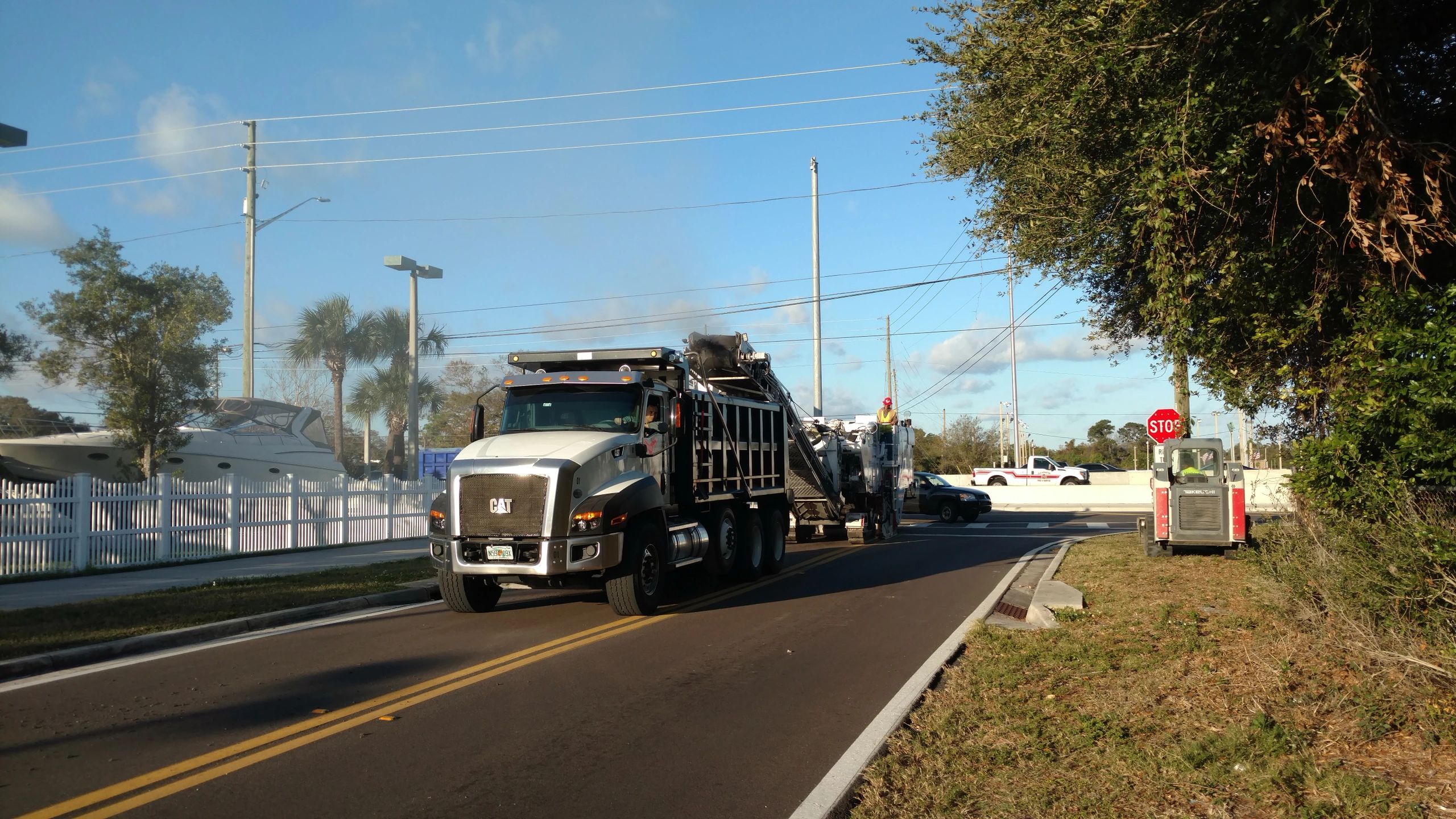 A large CAT truck on a street near boats and trees on a clear day.
