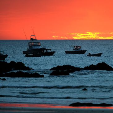 Boats on the ocean at sunset with an orange sky.