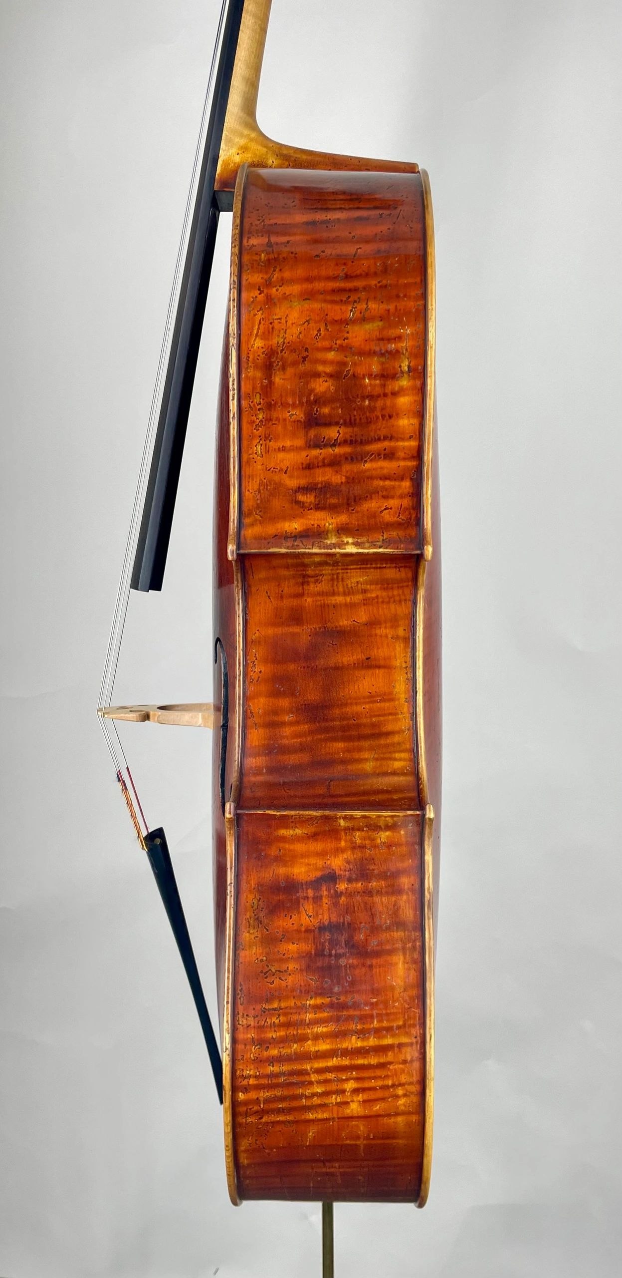 Side view of a polished wooden cello with bow against a plain background.