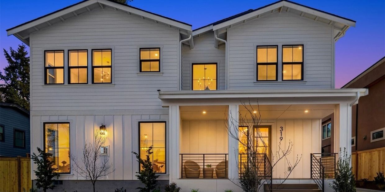 Modern two-story white house with illuminated windows at dusk.