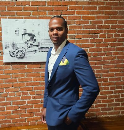 Man in a blue suit posing against a brick wall with vintage photo.